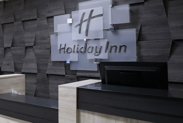 A Holiday Inn reception desk with a modern design, featuring a dark wood panel wall and a sleek black counter.