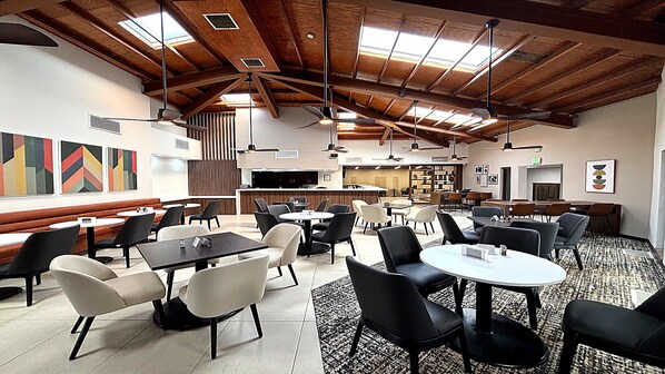 A spacious dining area with high ceilings and exposed beams, featuring multiple tables and chairs, a bar area, and artwork on the walls. - Holiday Inn & Suites Chihuahua Expo (Chihuahua)