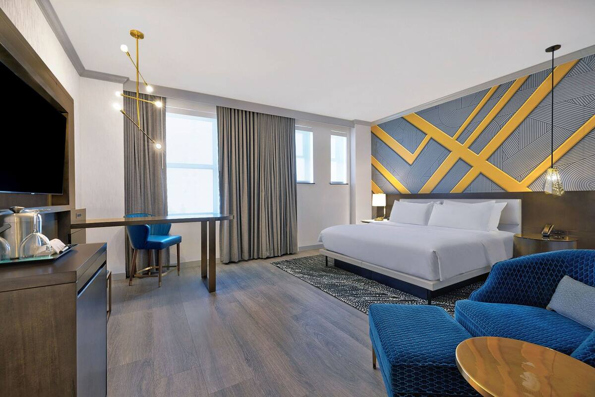 A modern hotel room with a bed, a desk, a blue sofa, and a TV.
