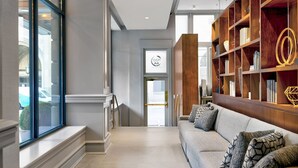 A modern hotel lobby with a sofa, bookshelves, and a view of the street. - Le Meridien St. Louis Downtown (St. Louis)