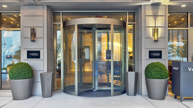 A revolving door with glass panels, two potted plants, and signage for 'MERIDEN' and 'VALET'. - Le Meridien St. Louis Downtown (St. Louis)