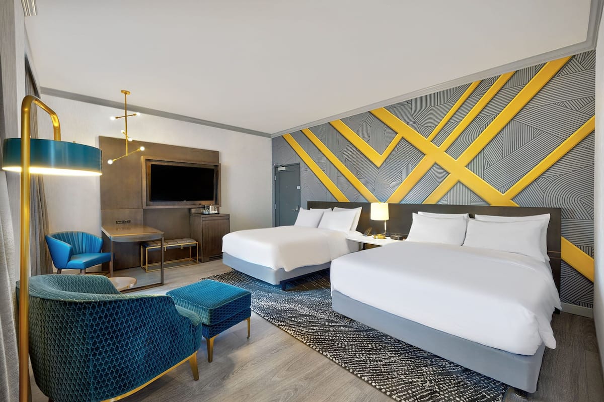 A hotel room with two beds, a desk, a chair, and a TV.