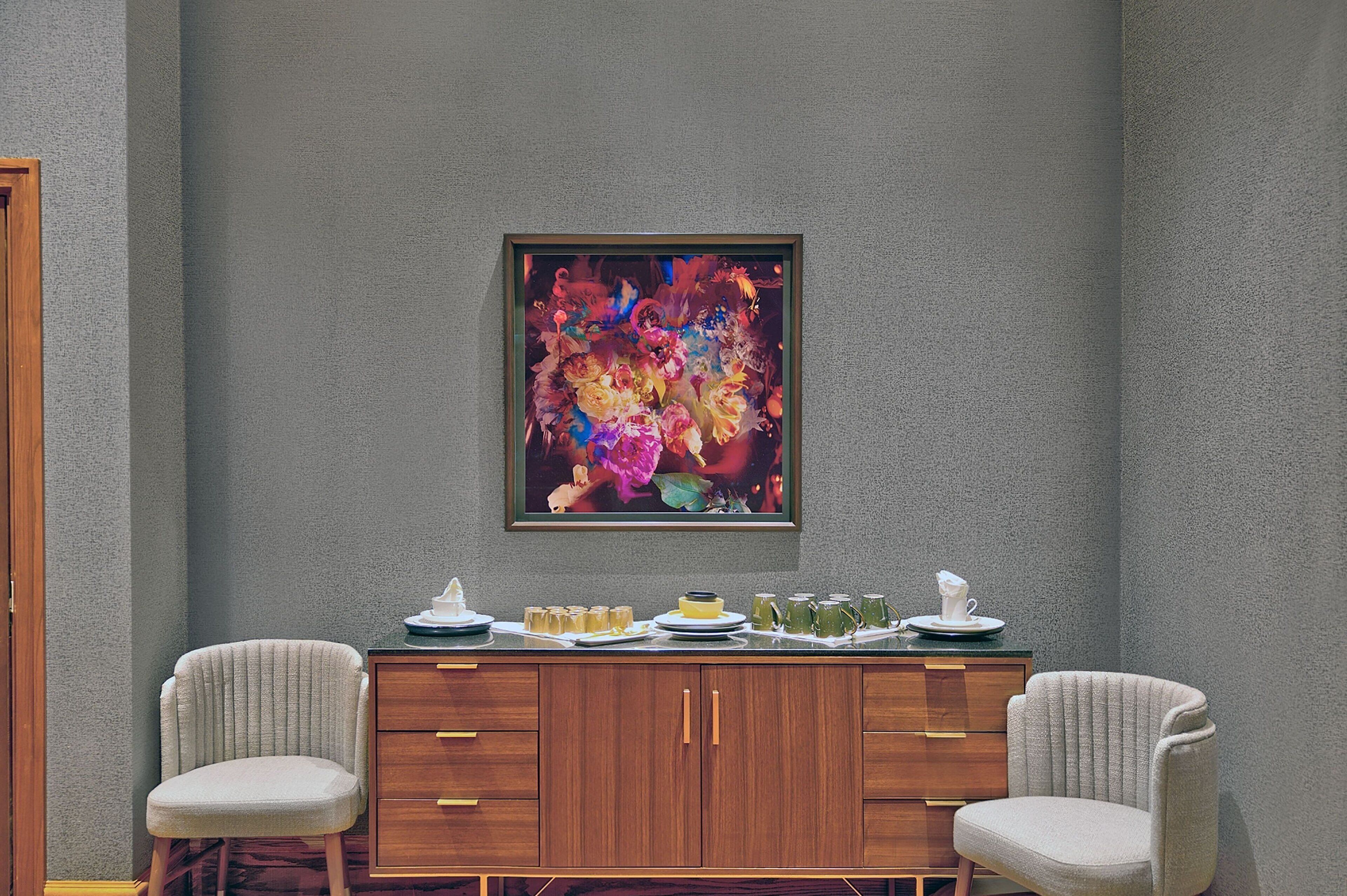 A dining area with a wooden cabinet and two chairs, a colorful abstract painting on the wall, and a table set with plates, glasses, and a pitcher.