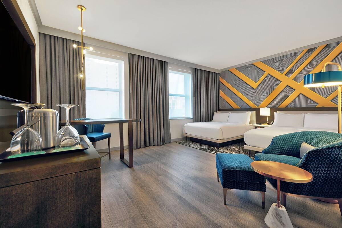 A modern hotel room with a large bed, a sofa, a small table, a TV, and a desk with a lamp.