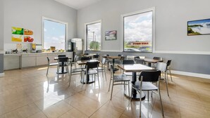 A modern dining area with multiple tables and chairs, large windows, and a kitchen counter with various items. - Quality Inn - Niagara Falls Blvd (Niagara Falls)