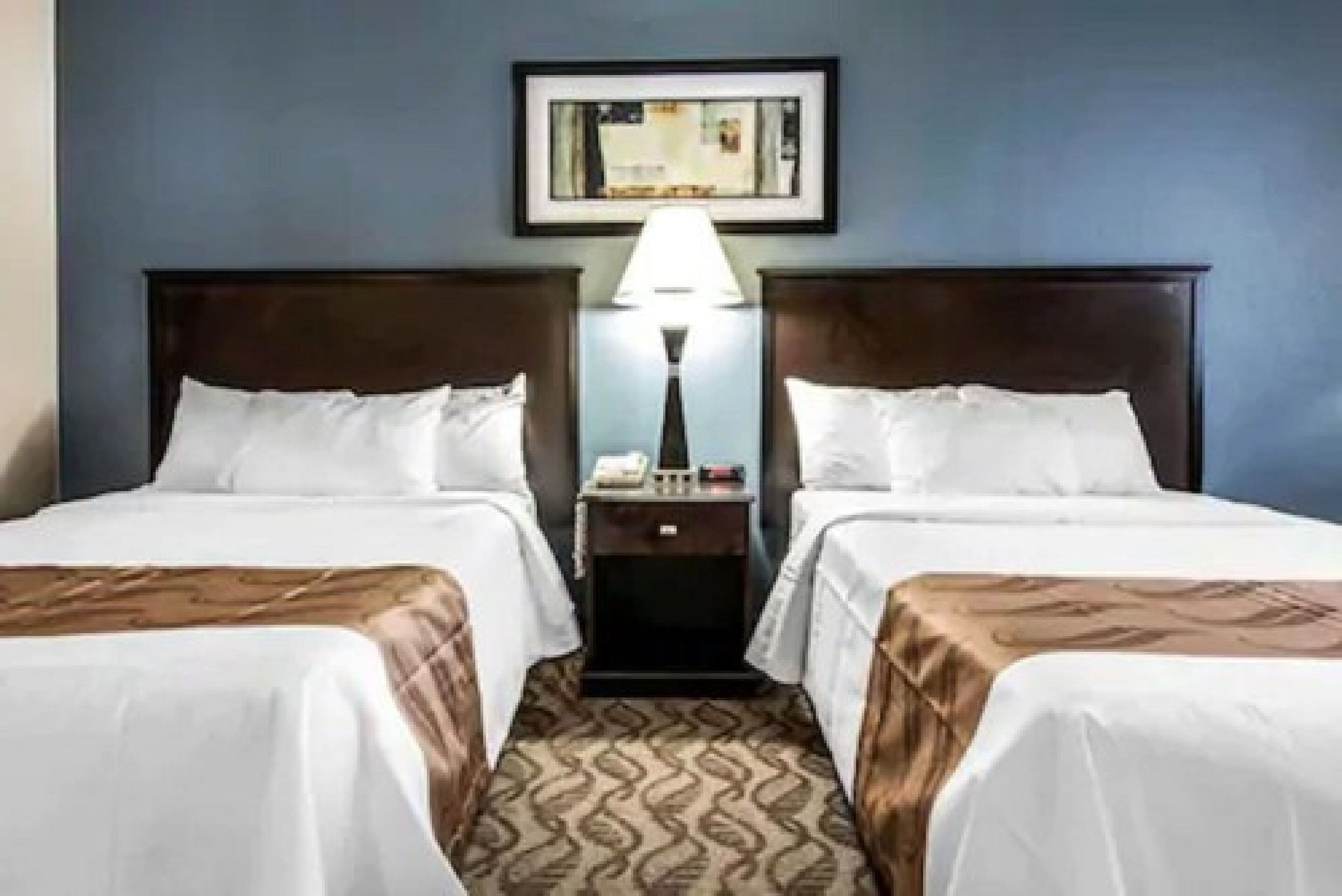 A hotel room with two single beds, a nightstand with a lamp, and a framed picture on the wall.