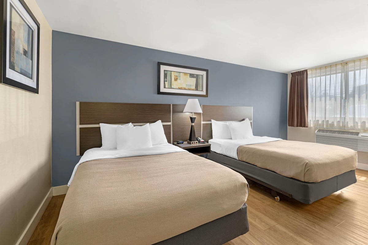 Une chambre d’hôtel avec deux lits, une table de chevet, une lampe et un tableau encadré au mur.