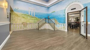 A room with a mural of a coastal scene, a staircase, and a view into a dining area. - Quality Inn - Niagara Falls Blvd (Niagara Falls)