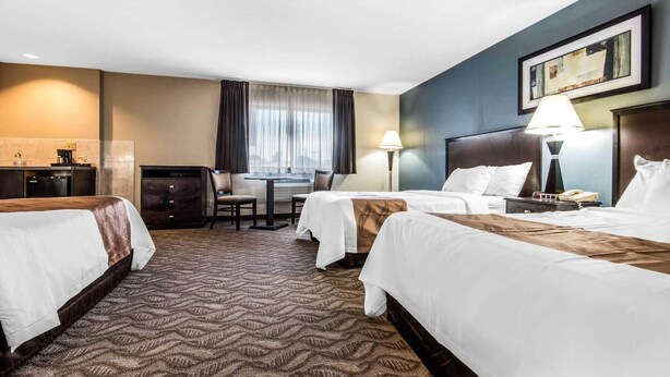 A hotel room with two beds, a desk, a chair, a lamp, and a painting on the wall. - Quality Inn - Niagara Falls Blvd (Niagara Falls)