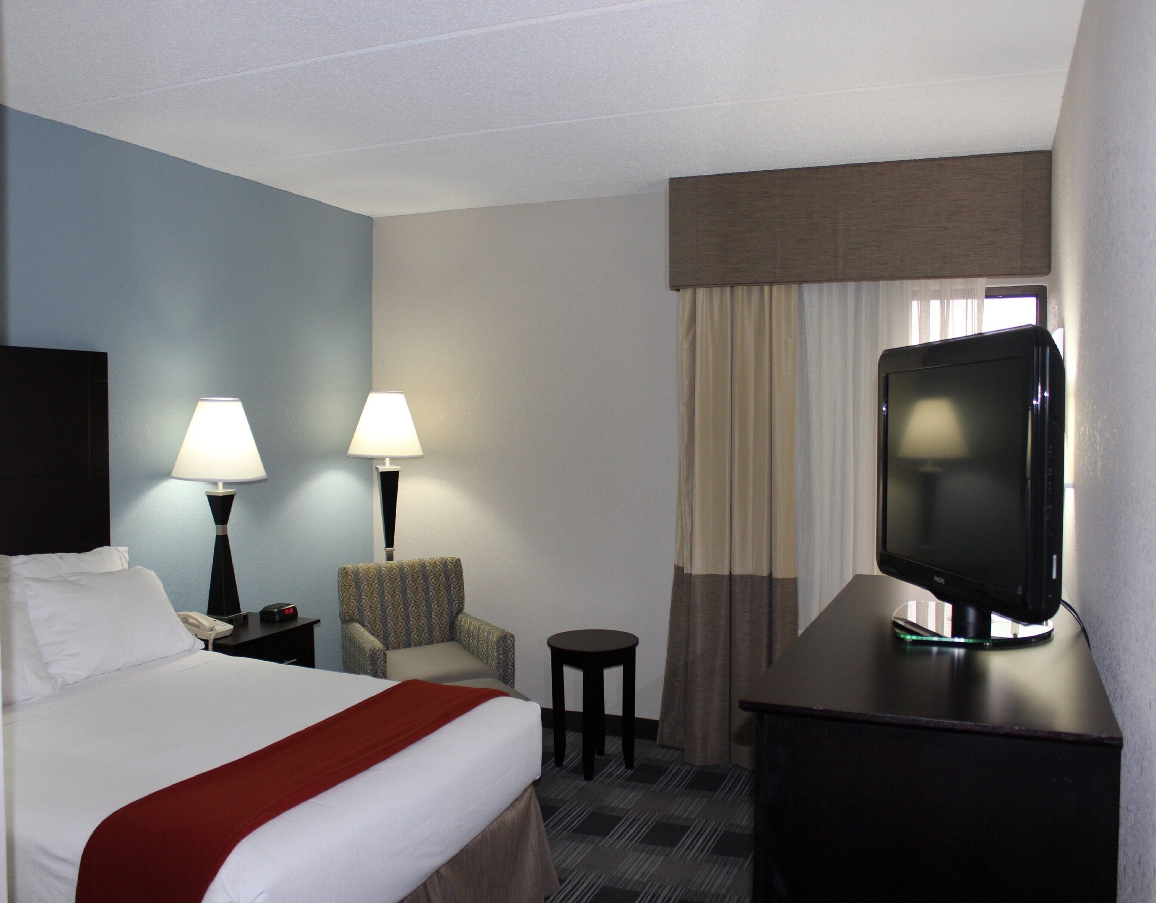 A hotel room with a bed, two bedside lamps, a television on a desk, a chair, and a small table.