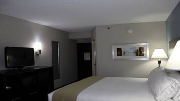 A hotel room with a bed, a television on a stand, a lamp, and a framed picture on the wall.