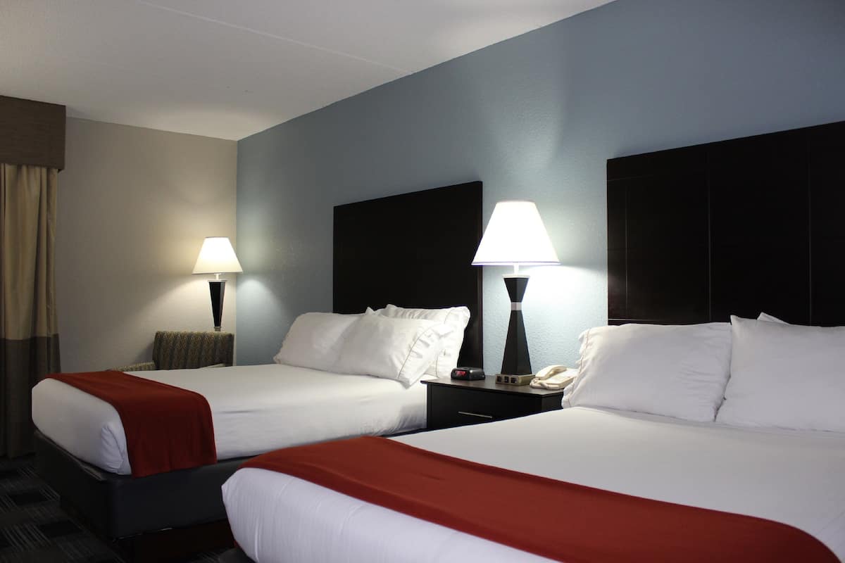 A hotel room with two beds, each with white linens and red throw blankets. There are bedside tables with lamps and a telephone.