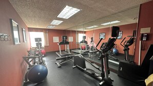Une salle de sport équipée de matériel d’exercice, dotée d’un grand miroir et d’un mur rouge.