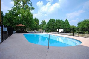 A swimming pool with a curved edge, surrounded by a fence, and trees in the background.