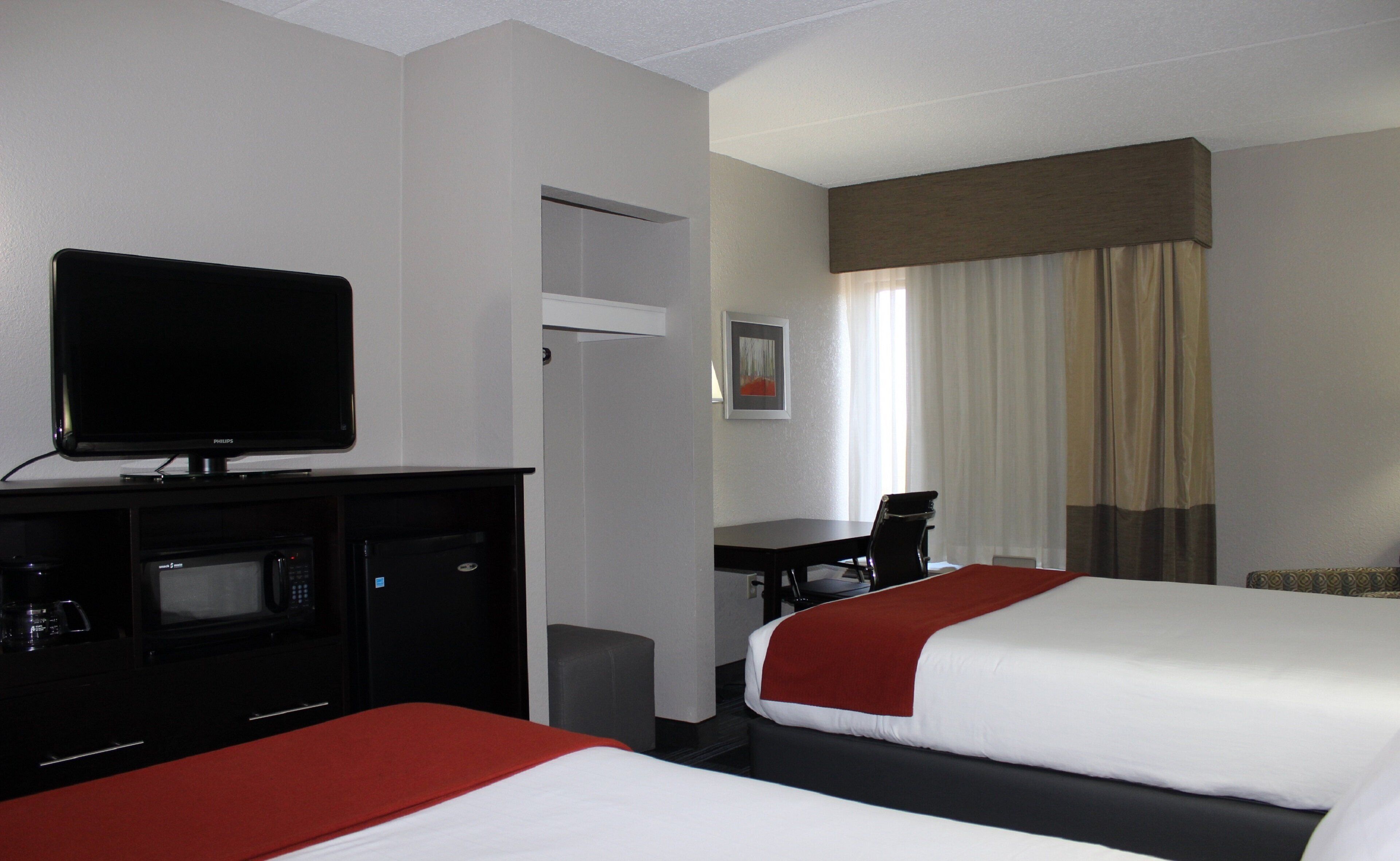 A hotel room with two beds, a desk, a television, and a minibar.