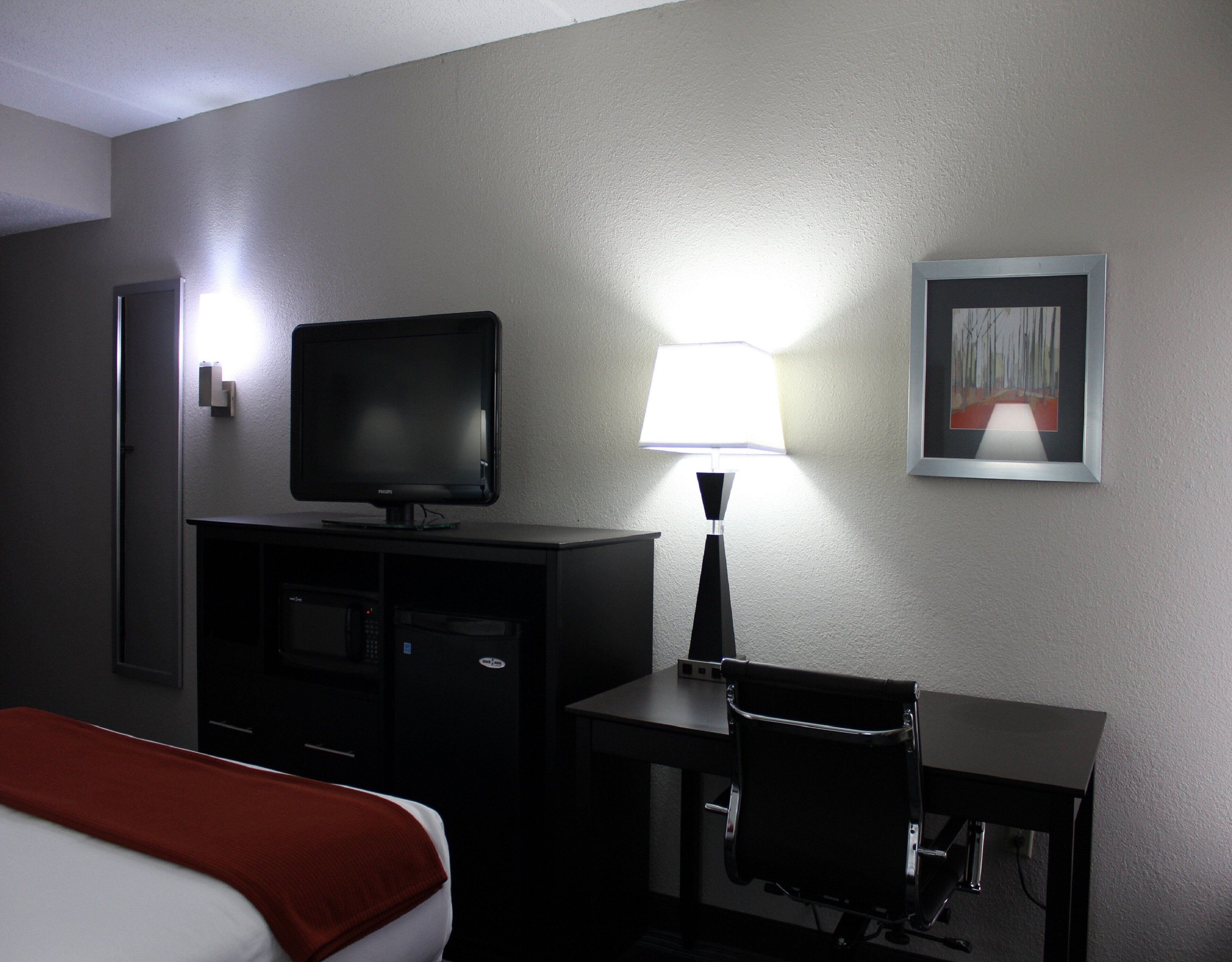 A hotel room with a bed, a desk, a television, a lamp, and a framed picture on the wall.