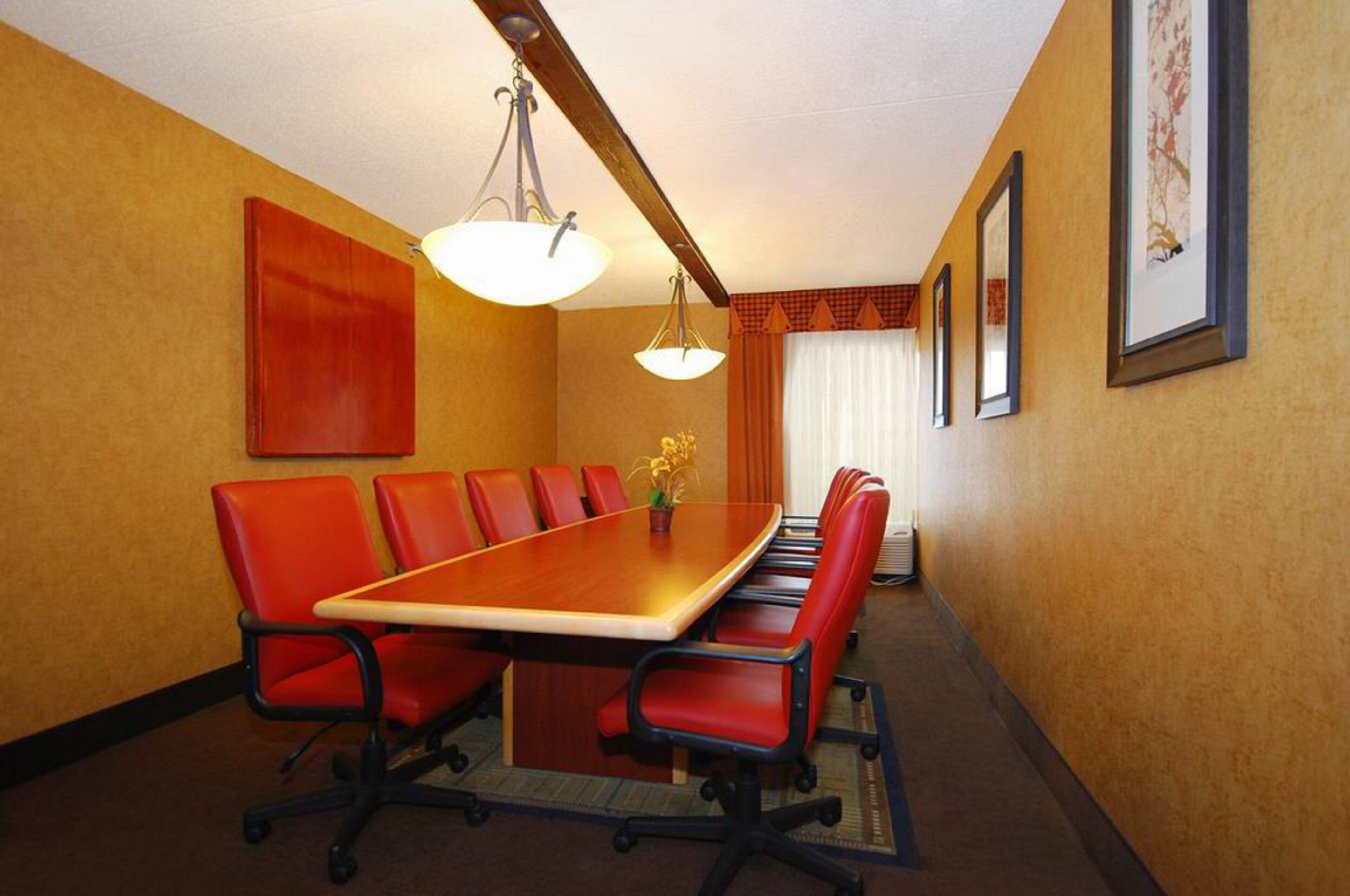 A conference room with a long table and red chairs, a chandelier, and framed pictures on the wall.