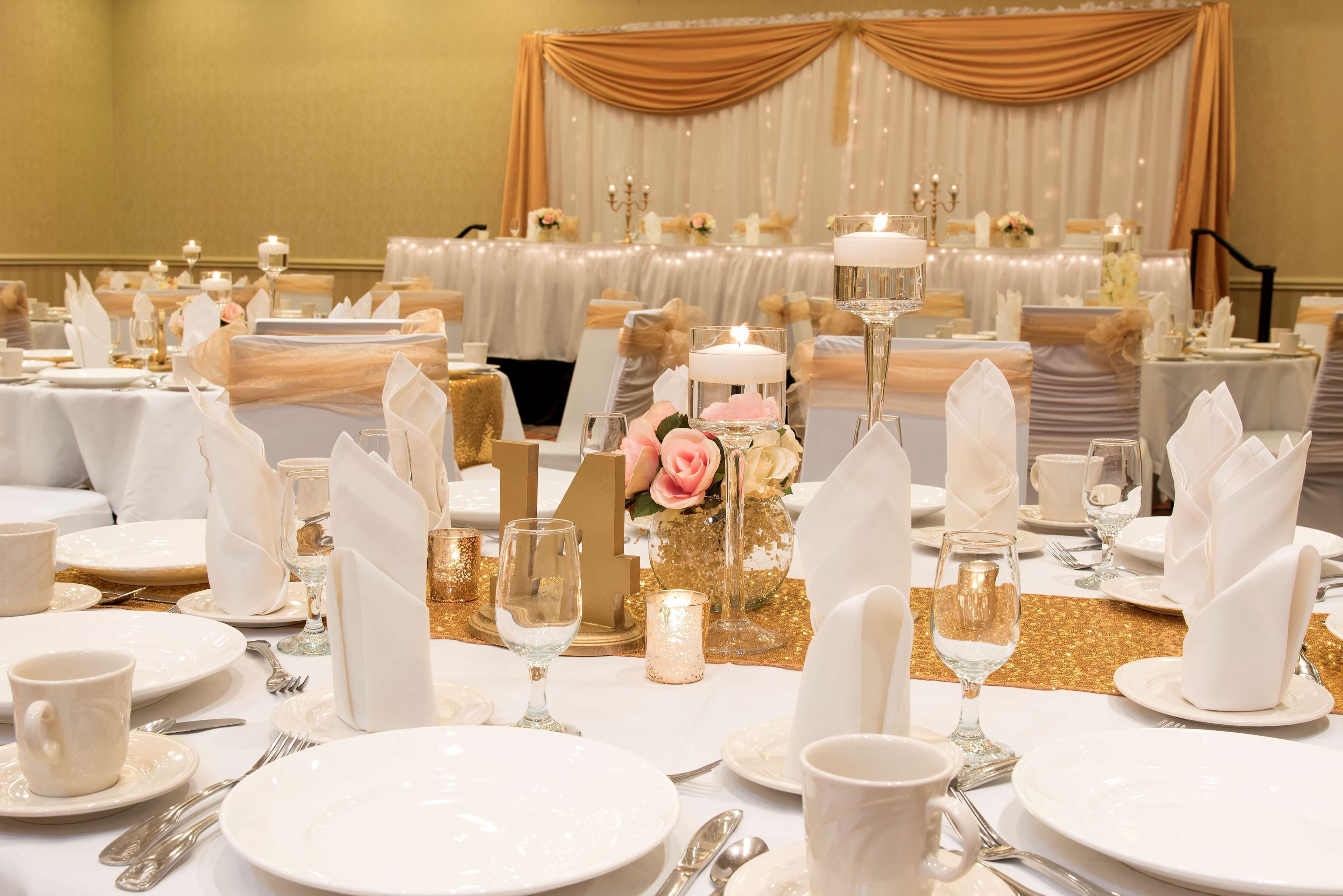 A banquet hall with round tables set for a formal event, featuring white tablecloths, gold accents, and floral centerpieces.