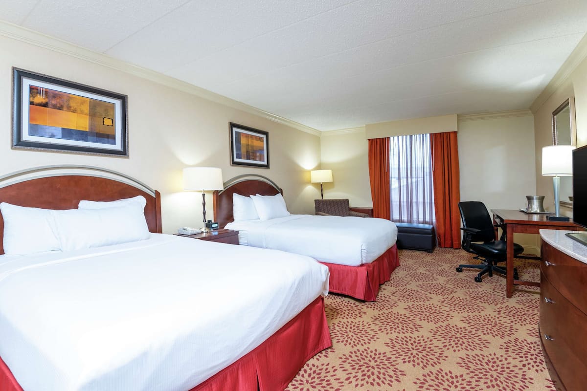 A hotel room with two beds, a desk, a chair, and a TV.