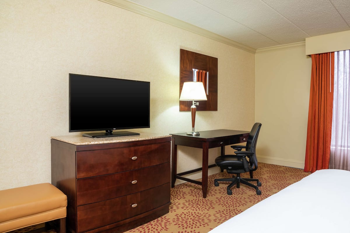 A hotel room with a bed, a desk with a chair, a television, a lamp, and a dresser.