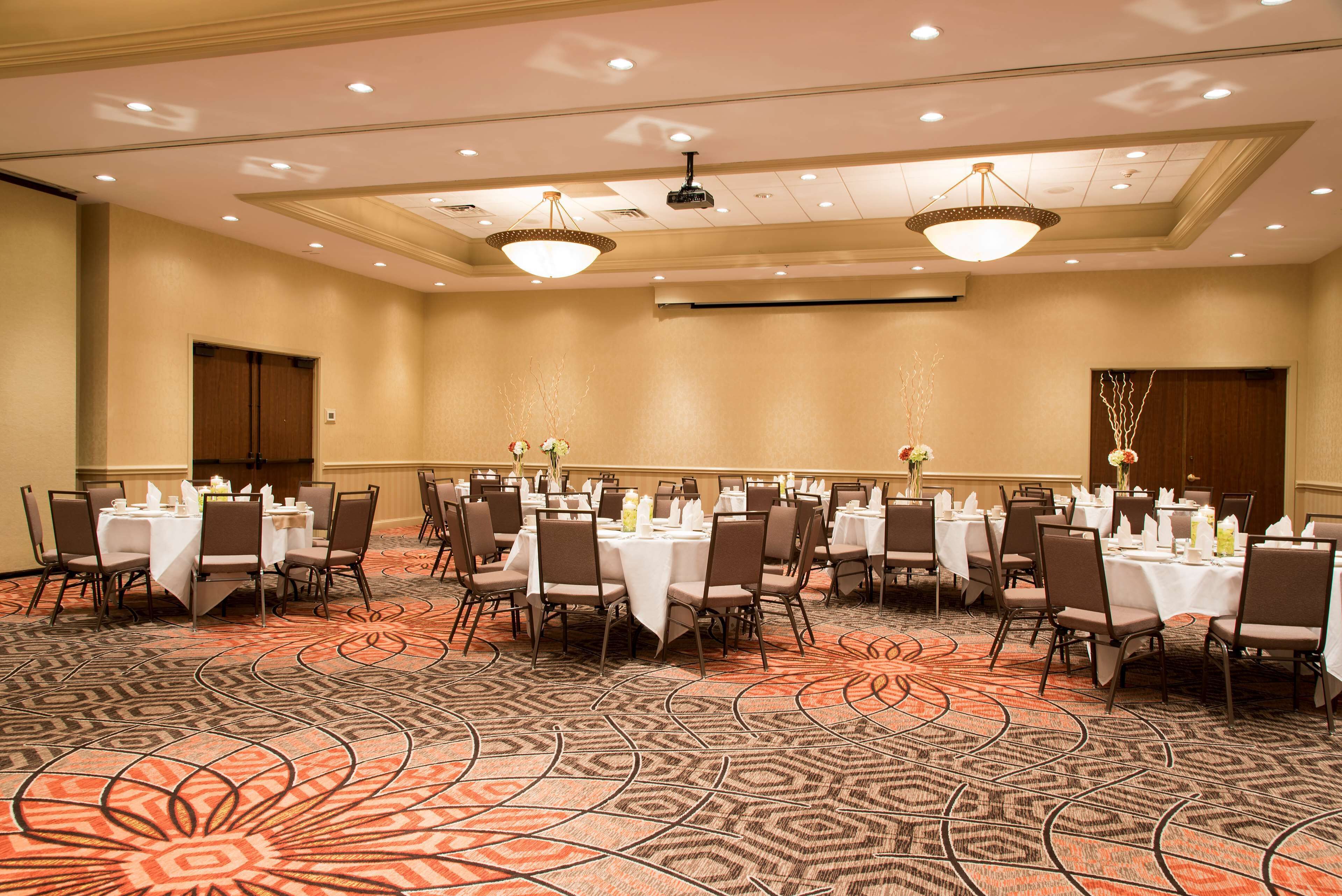 A conference room with multiple tables set for dining, arranged in rows with chairs.