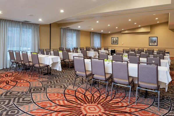A conference room with multiple tables and chairs, large windows with curtains, and a patterned carpet. - DoubleTree by Hilton Hotel Grand Rapids Airport (Grand Rapids)