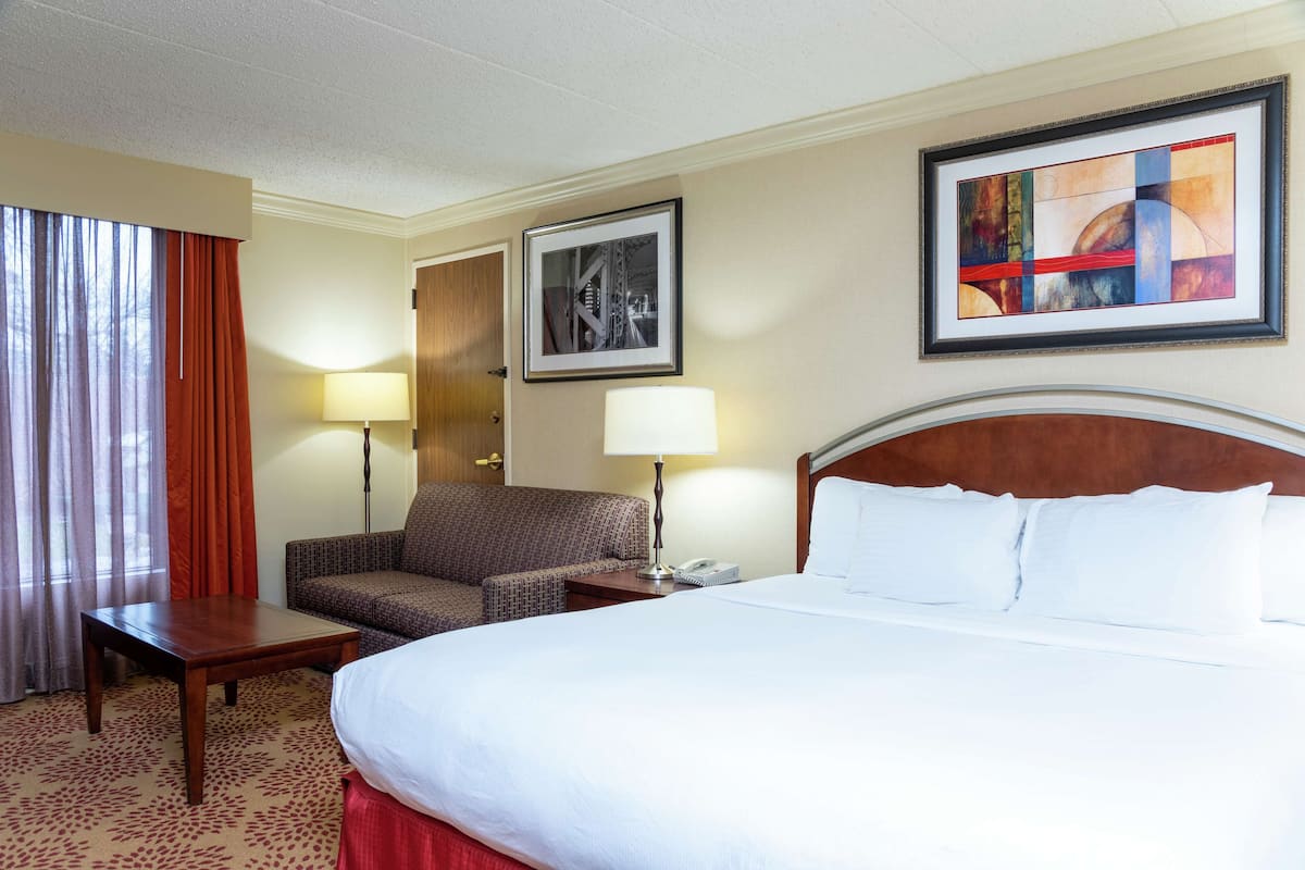 A hotel room with a large bed, a sofa, a desk, and two lamps.