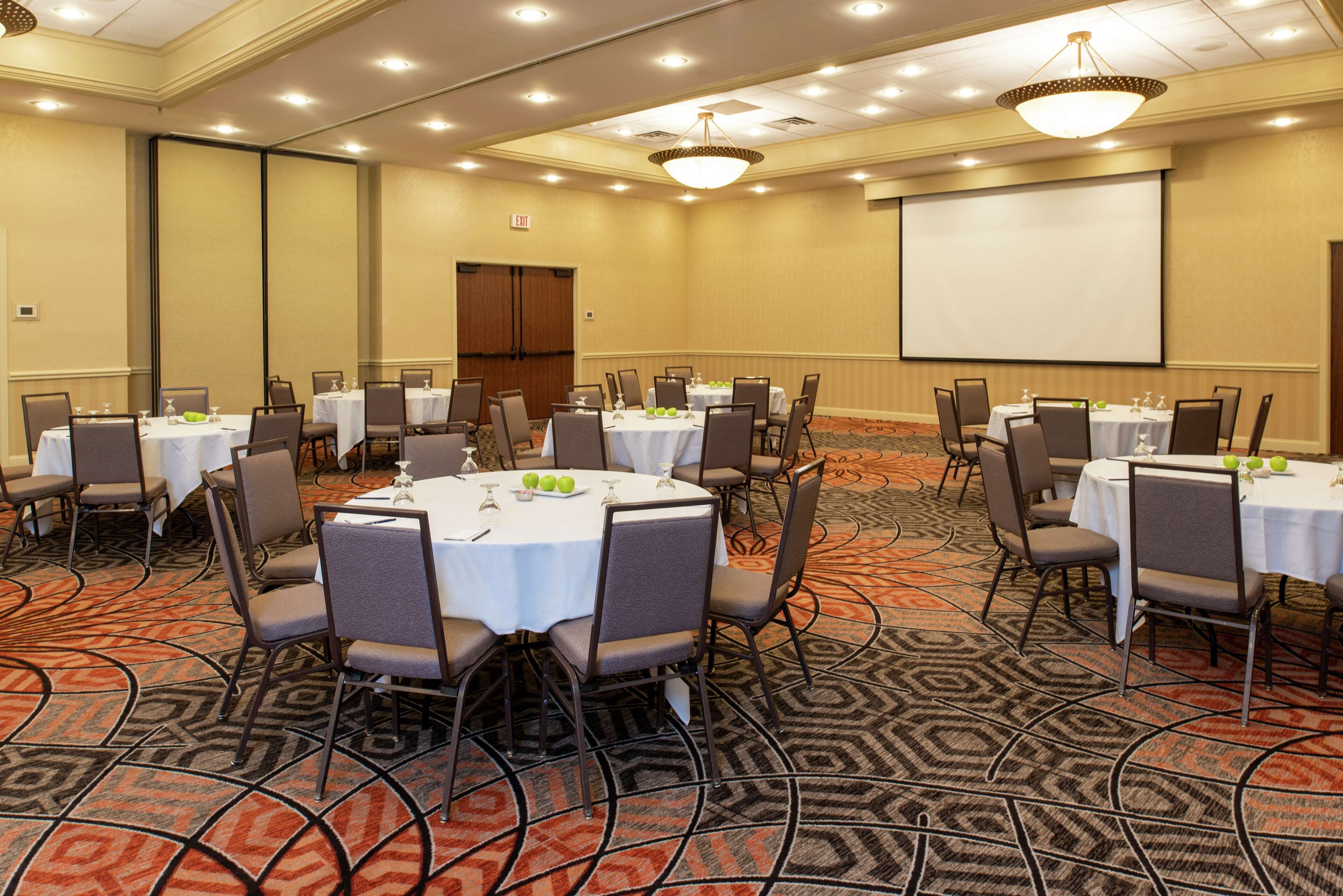 A conference room with round tables, chairs, and a projector screen.