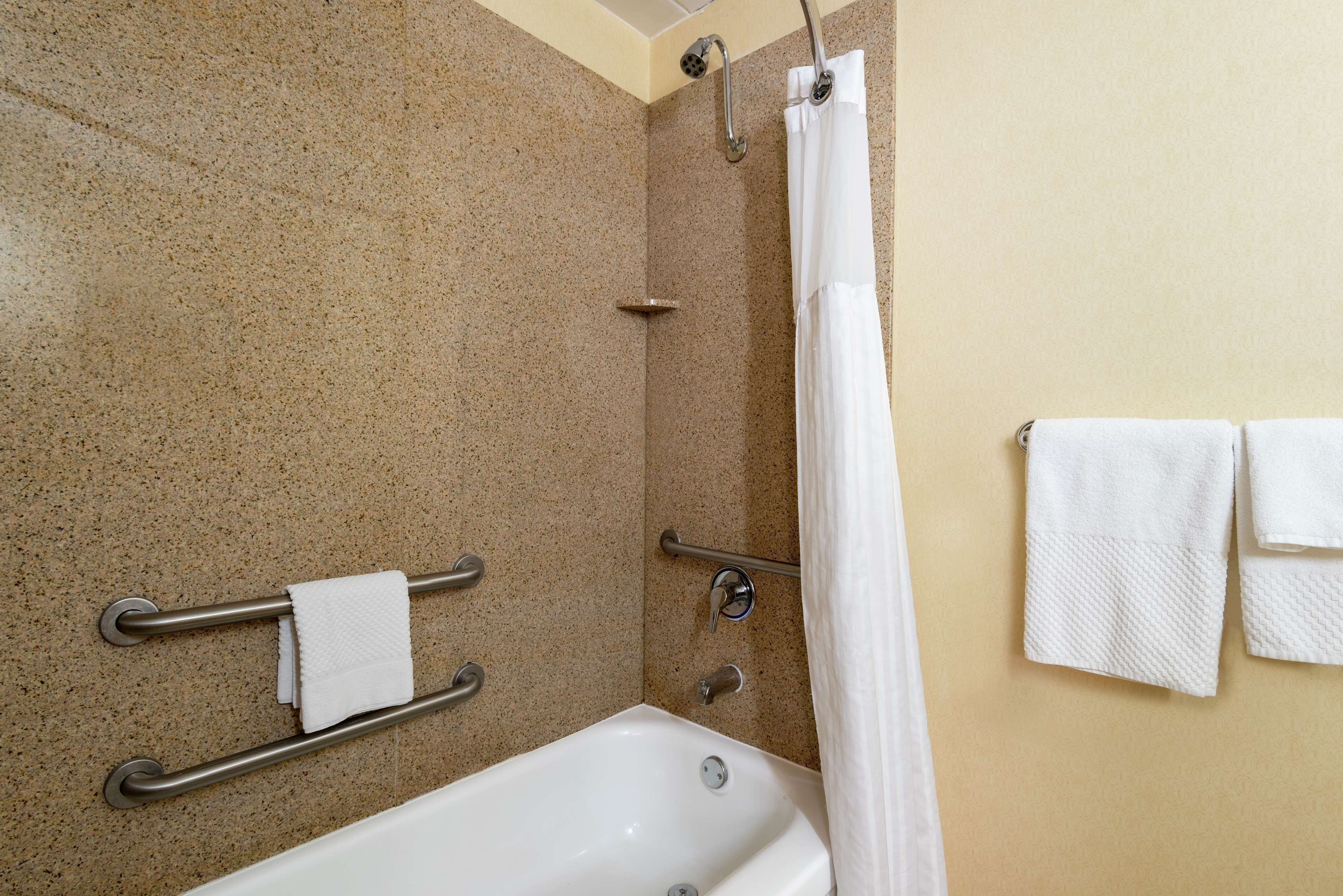 A bathroom with a bathtub, a shower with a glass door, a towel rack with towels, and a grab bar for safety.