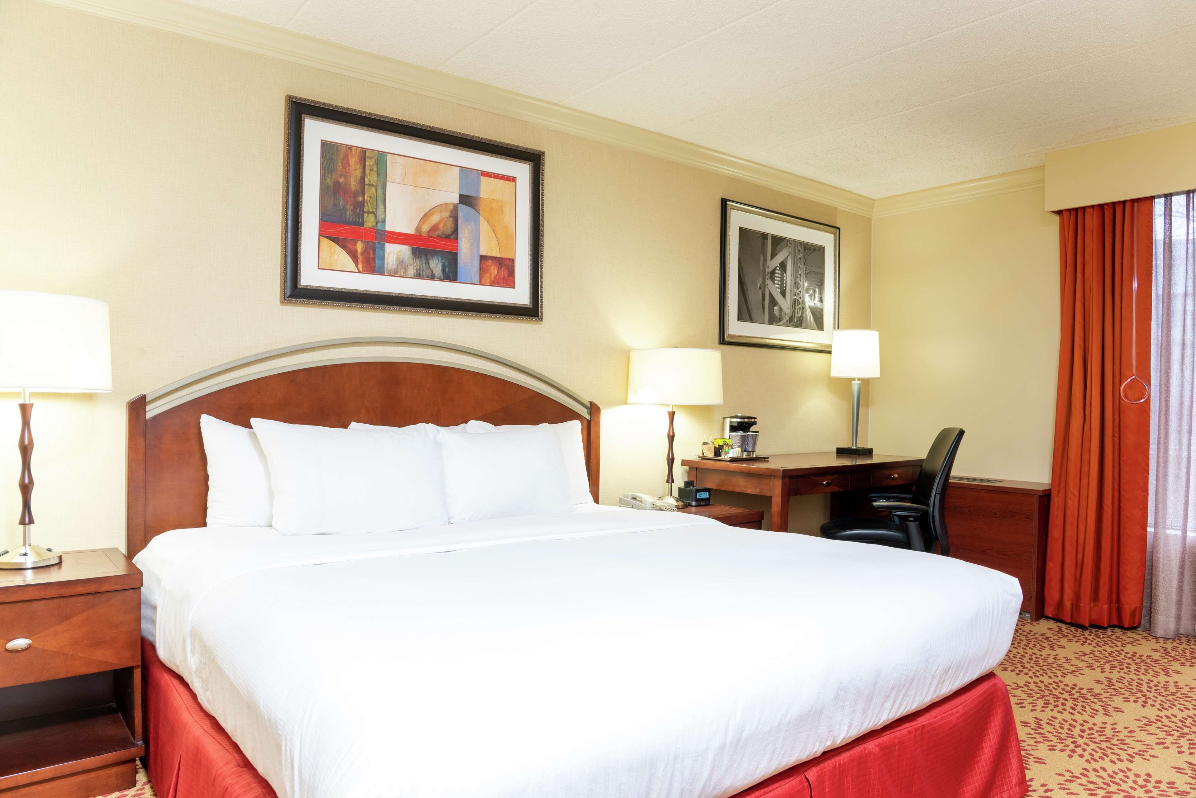 Una habitación de hotel con una cama grande, dos mesitas de noche, un escritorio con una silla y dos lámparas.
