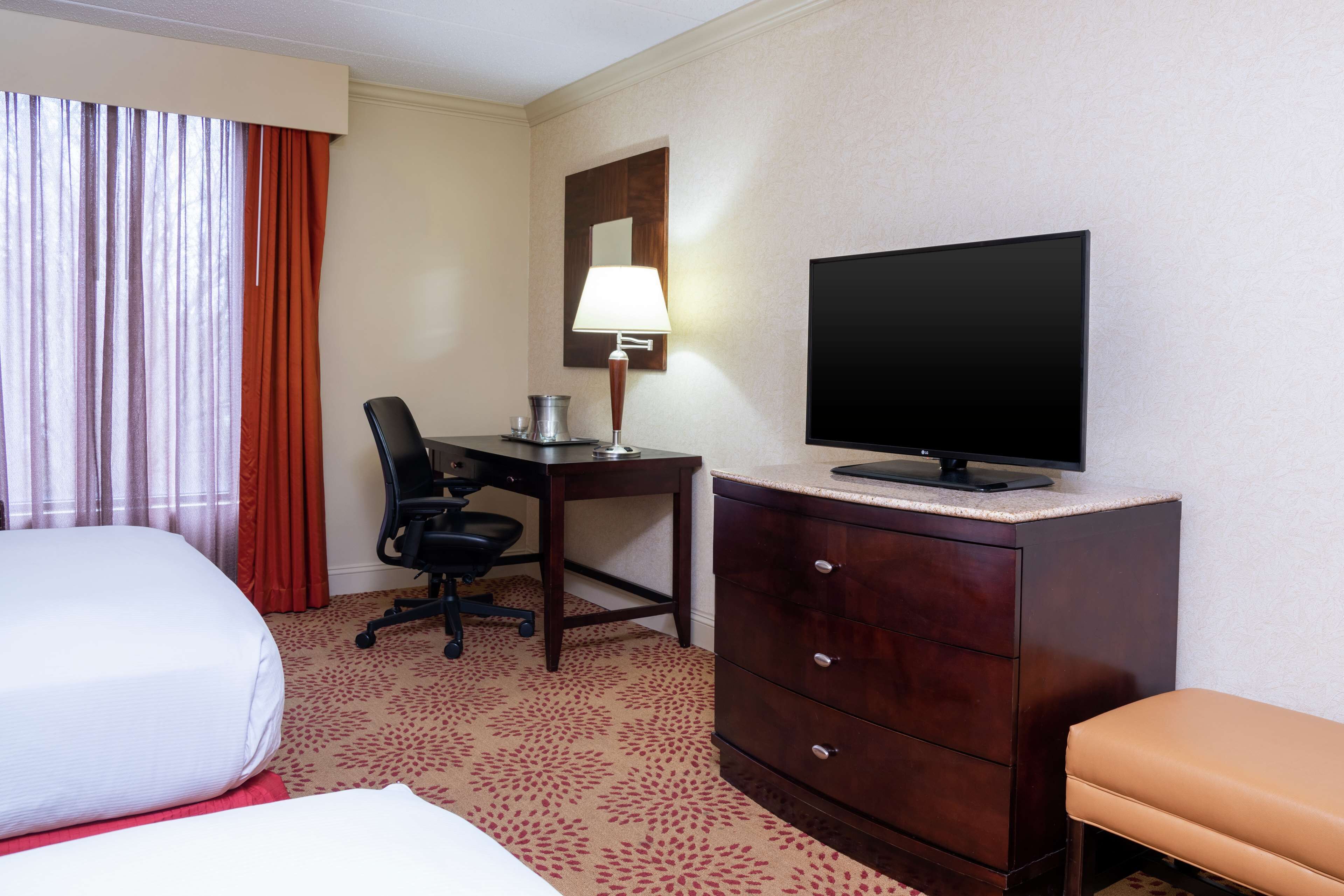 Una habitación de hotel con cama, escritorio con lámpara, televisión, silla y cómoda.