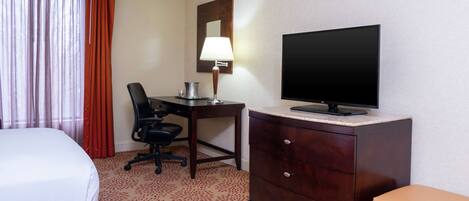 Una habitación de hotel con cama, escritorio con lámpara, televisión, silla y cómoda.