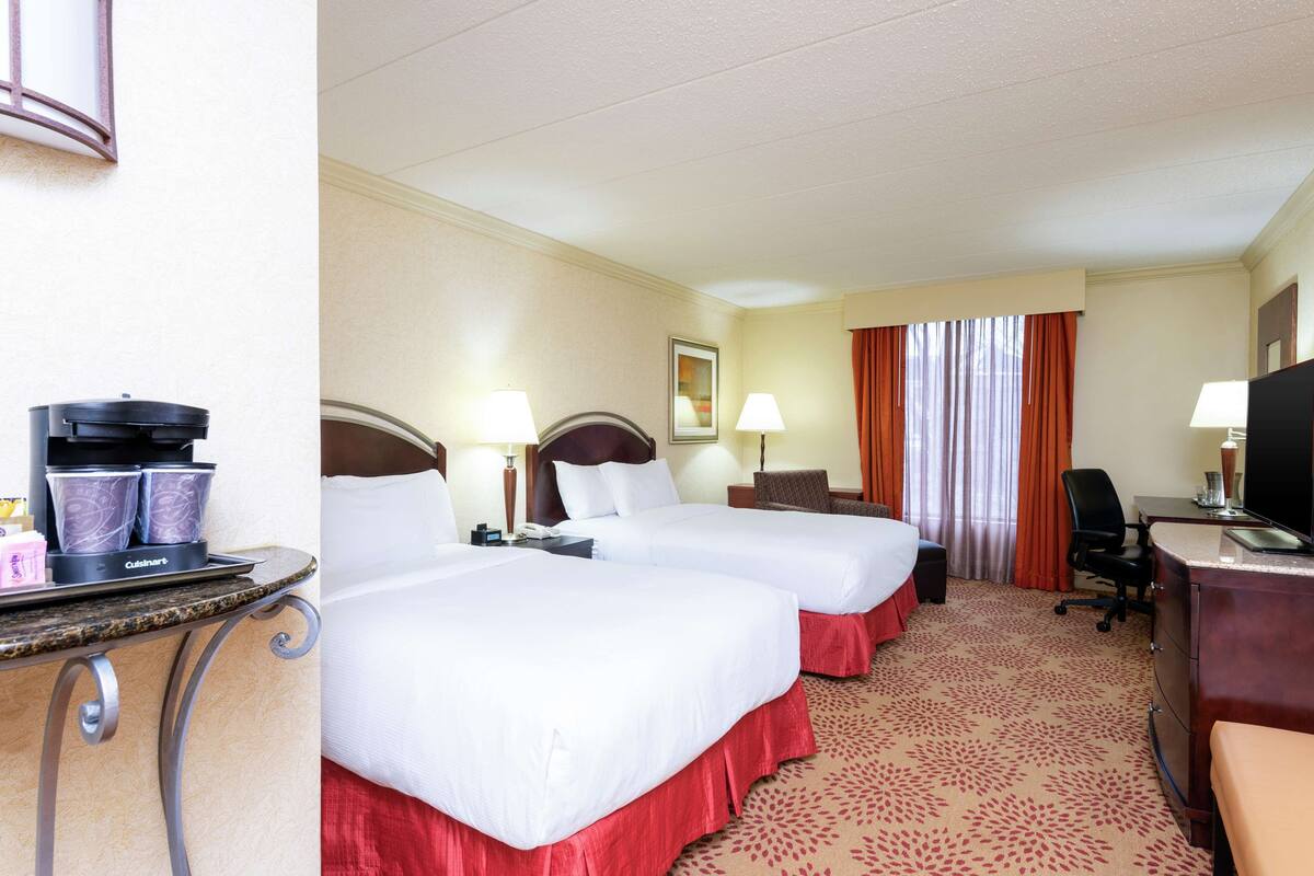 A hotel room with two beds, a desk with a computer, a chair, and a coffee machine.