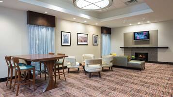 A hotel room with a dining table, chairs, a sofa, a TV, and a fireplace.