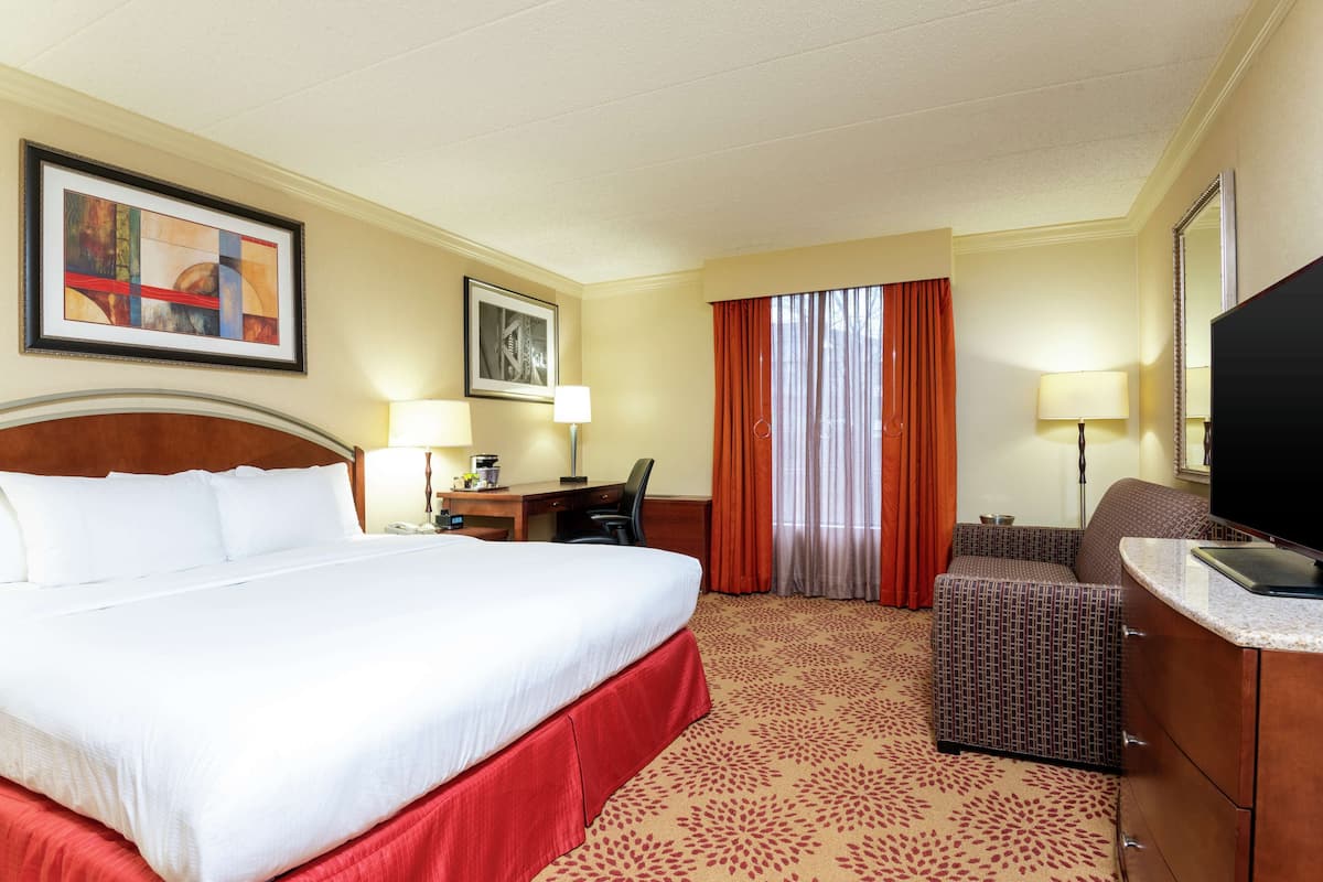 A hotel room with a large bed, a desk with a chair, a television, and a sofa.
