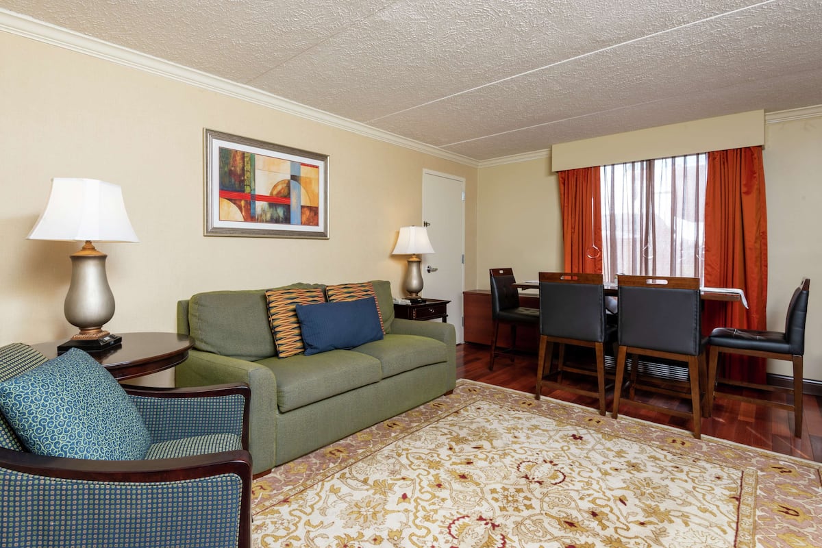 A living room with a green sofa, patterned rug, dining table with chairs, and two lamps.