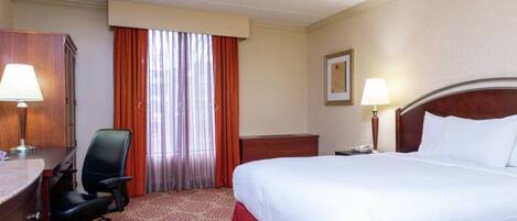 A hotel room with a bed, a desk, a chair, a lamp, and a window with curtains.