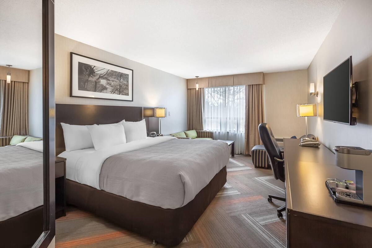 A hotel room with a large bed, bedside tables, a desk, a chair, a TV, and a framed picture on the wall.