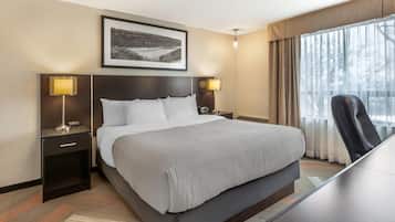 Quarto de hotel com uma cama grande, luminárias de cabeceira, uma escrivaninha e uma janela com cortinas.
