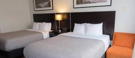 Una habitación de hotel con dos camas, una mesita de noche, una lámpara y una silla.