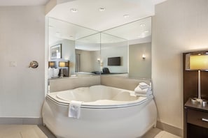 A modern bathroom with a large bathtub, a mirror, a television, and a lamp.
