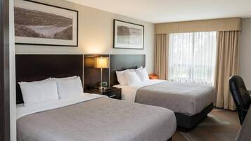 A hotel room with two beds, a nightstand with a lamp, a chair, and two framed pictures on the wall.