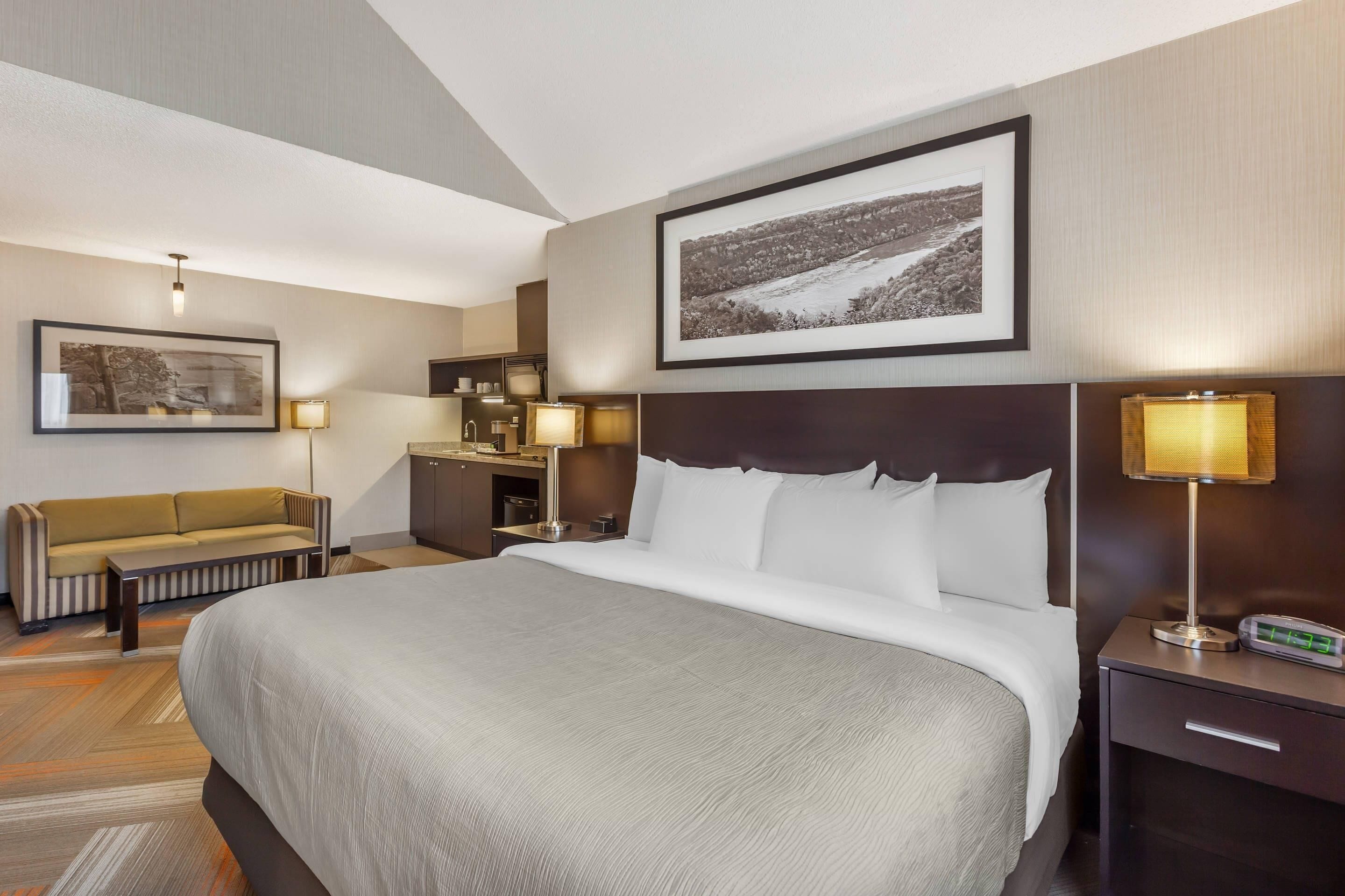 Een hotelkamer met een groot bed, een bank, een bureau met een lamp en een foto aan de muur.