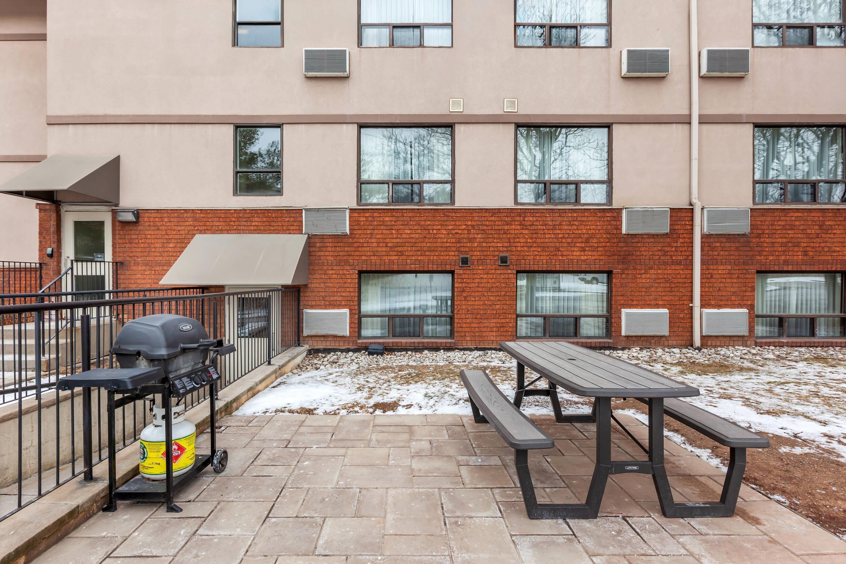 A patio with a grill, picnic table, and a brick building with multiple windows.