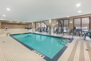 A swimming pool with a tiled deck, a lounge area with chairs, and a view through large windows. - Quality Hotel (Burlington)