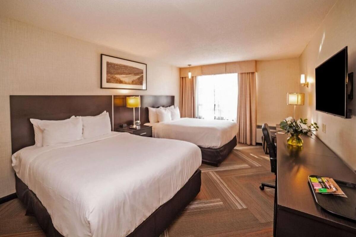 A hotel room with two beds, a desk, a TV, and a window with curtains.