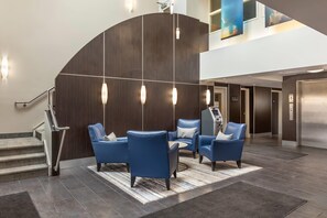 A lobby with a curved wall, a staircase, and a seating area with blue chairs. - Quality Hotel (Burlington)