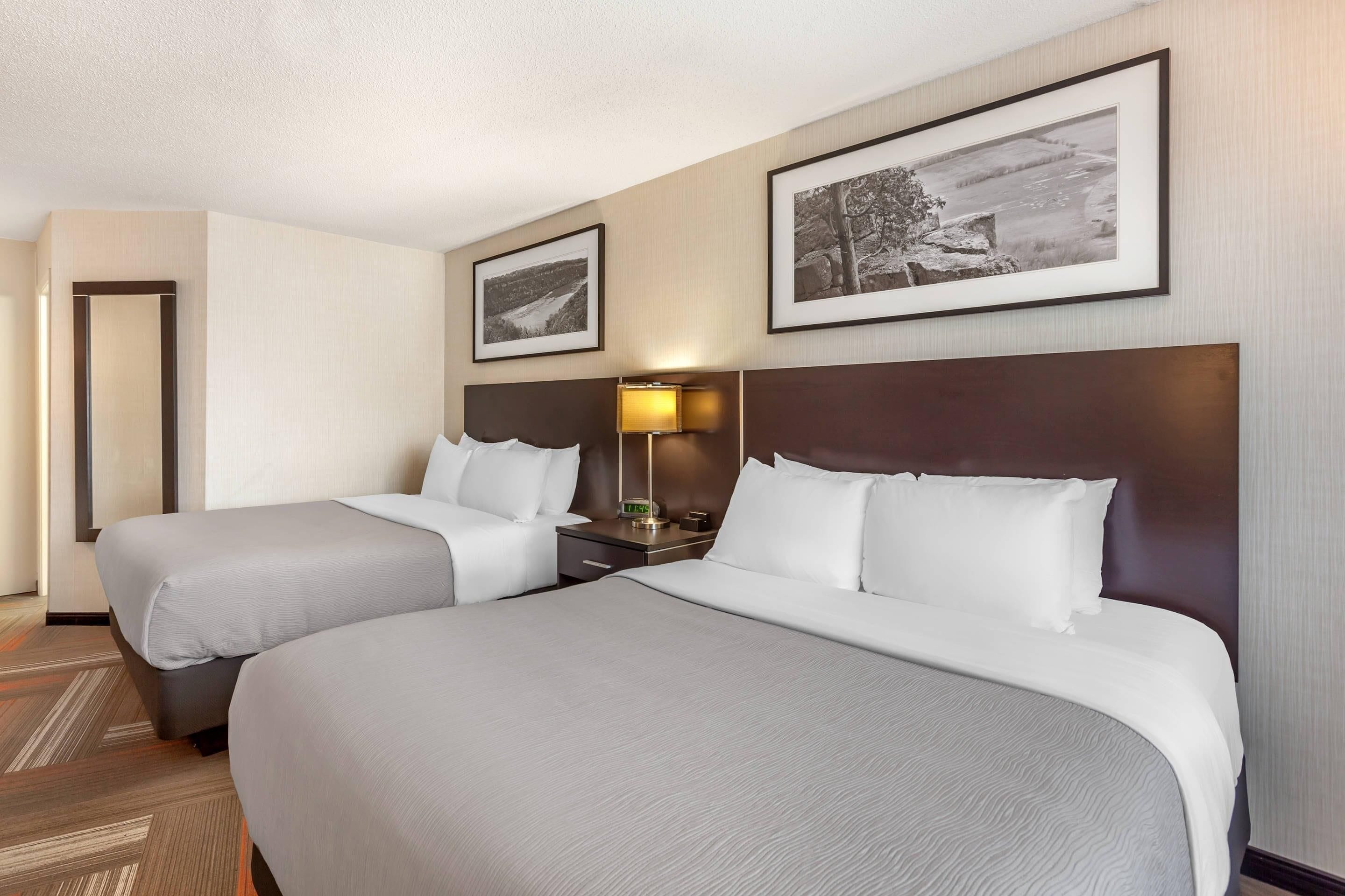 A hotel room with two beds, a nightstand with a lamp, and framed pictures on the wall.
