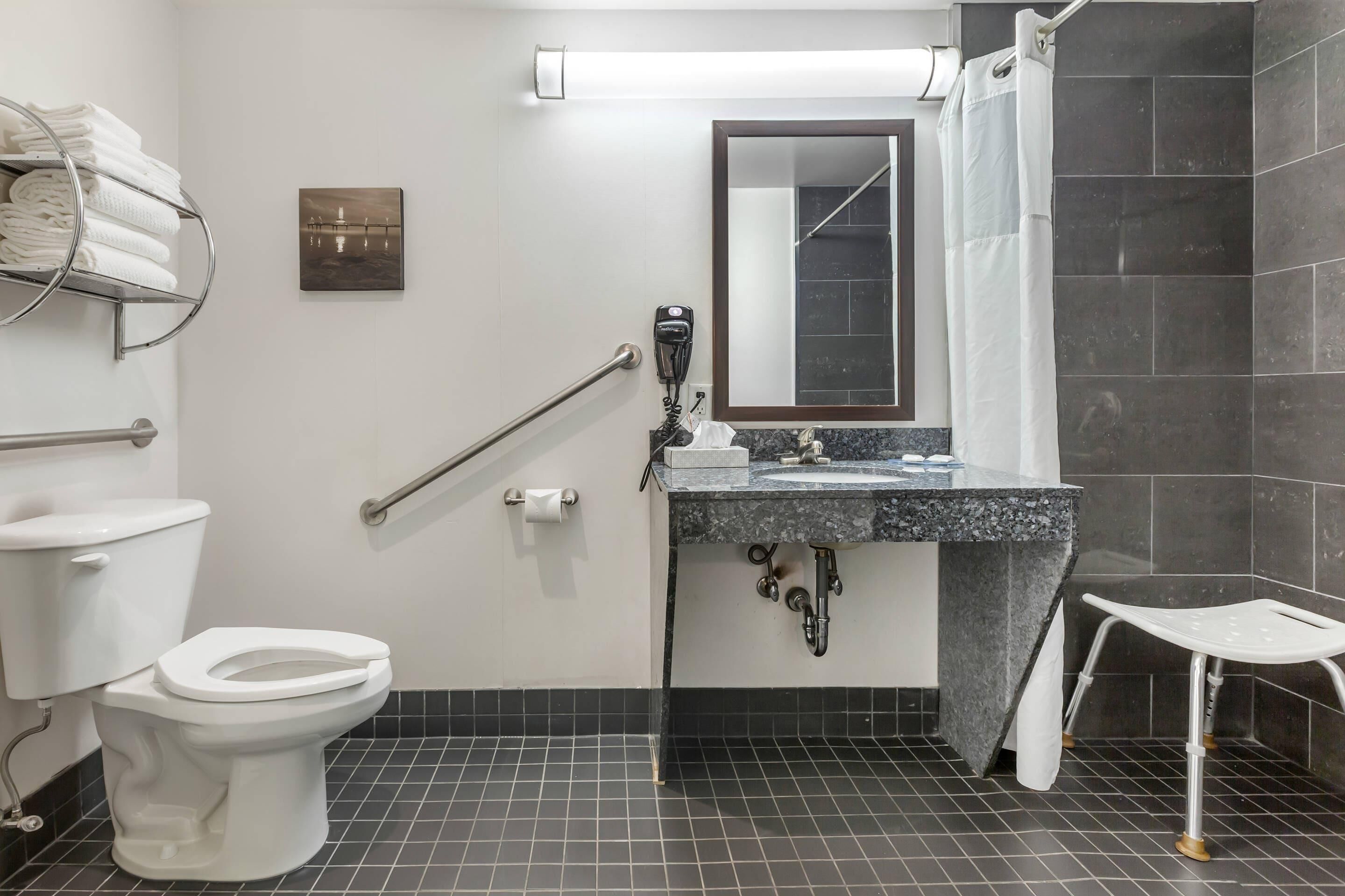 Un baño con inodoro, lavamanos, toallero, secamanos y cortina de ducha.