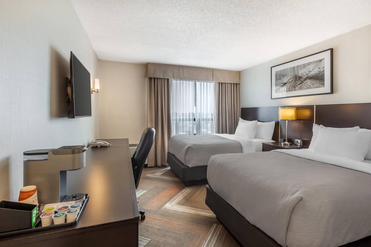 A hotel room with a bed, a desk with a coffee machine, a TV, and a window with curtains.